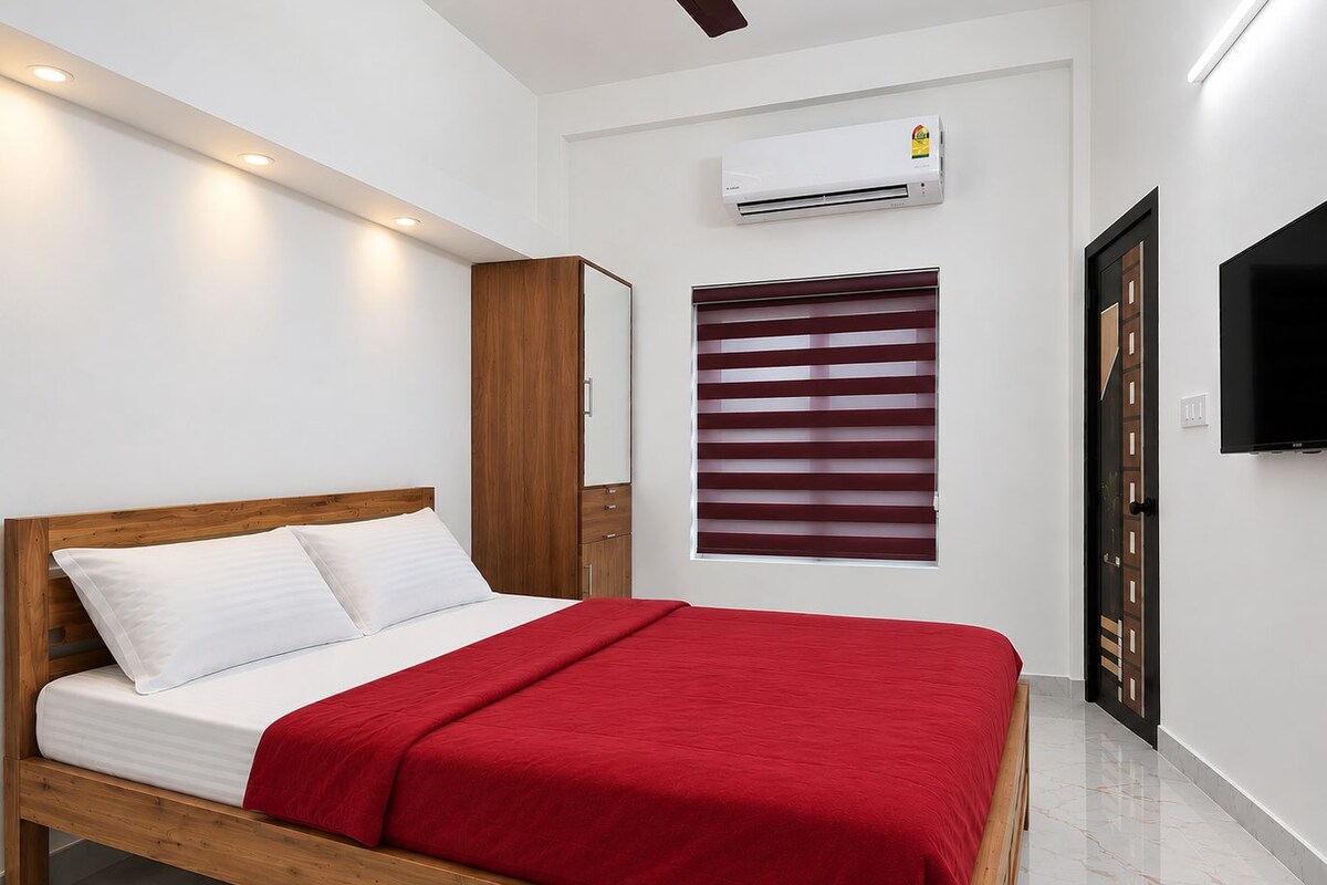 Ein Schlafzimmer mit einem hölzernen Bett, weißer Bettwäsche, einer roten Decke, einem Kleiderschrank, einer Klimaanlage, einem Fenster mit Jalousien und einem an der Wand befestigten Fernseher.