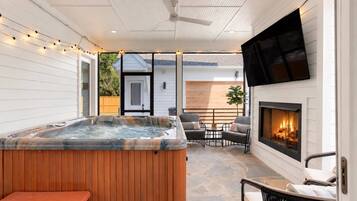 A hot tub with a wooden deck, a fireplace, and outdoor seating.