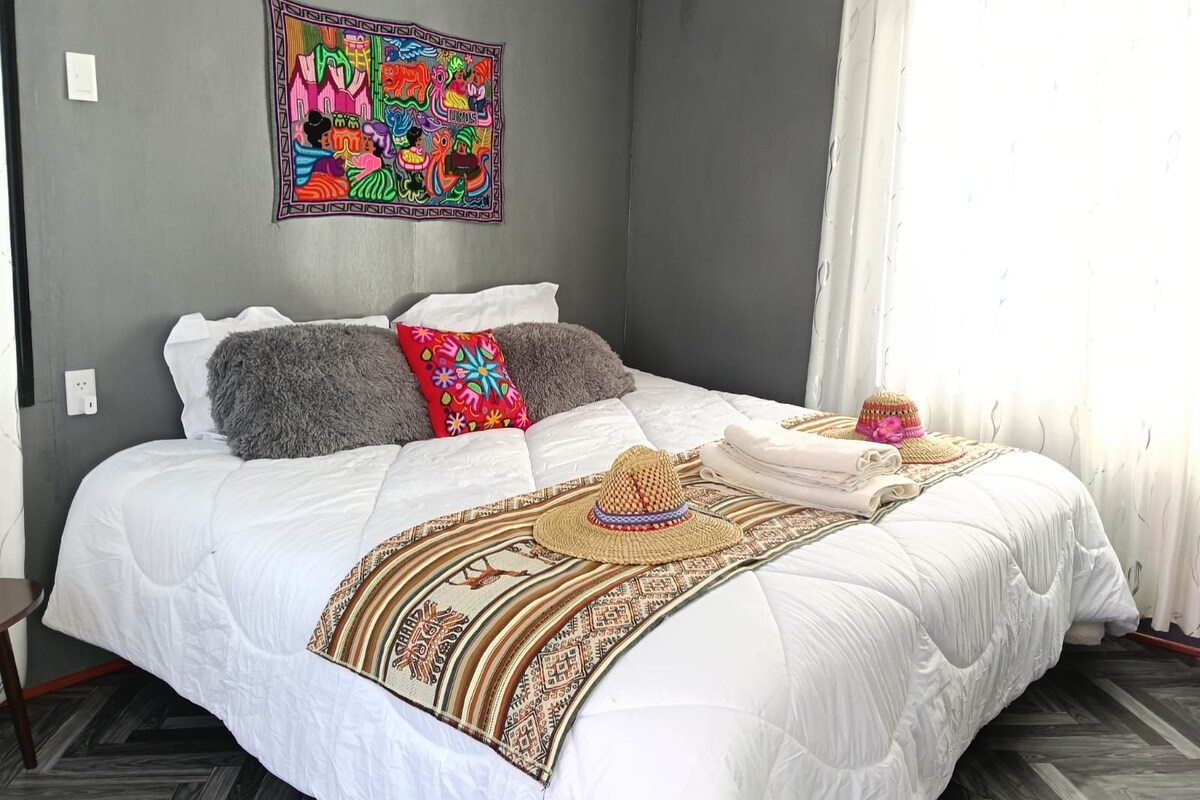 A bedroom with a bed, pillows, a blanket, and a wall hanging.