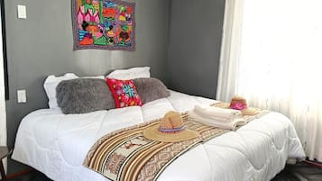Un dormitorio con cama, almohadas, una colcha y un tapiz en la pared.