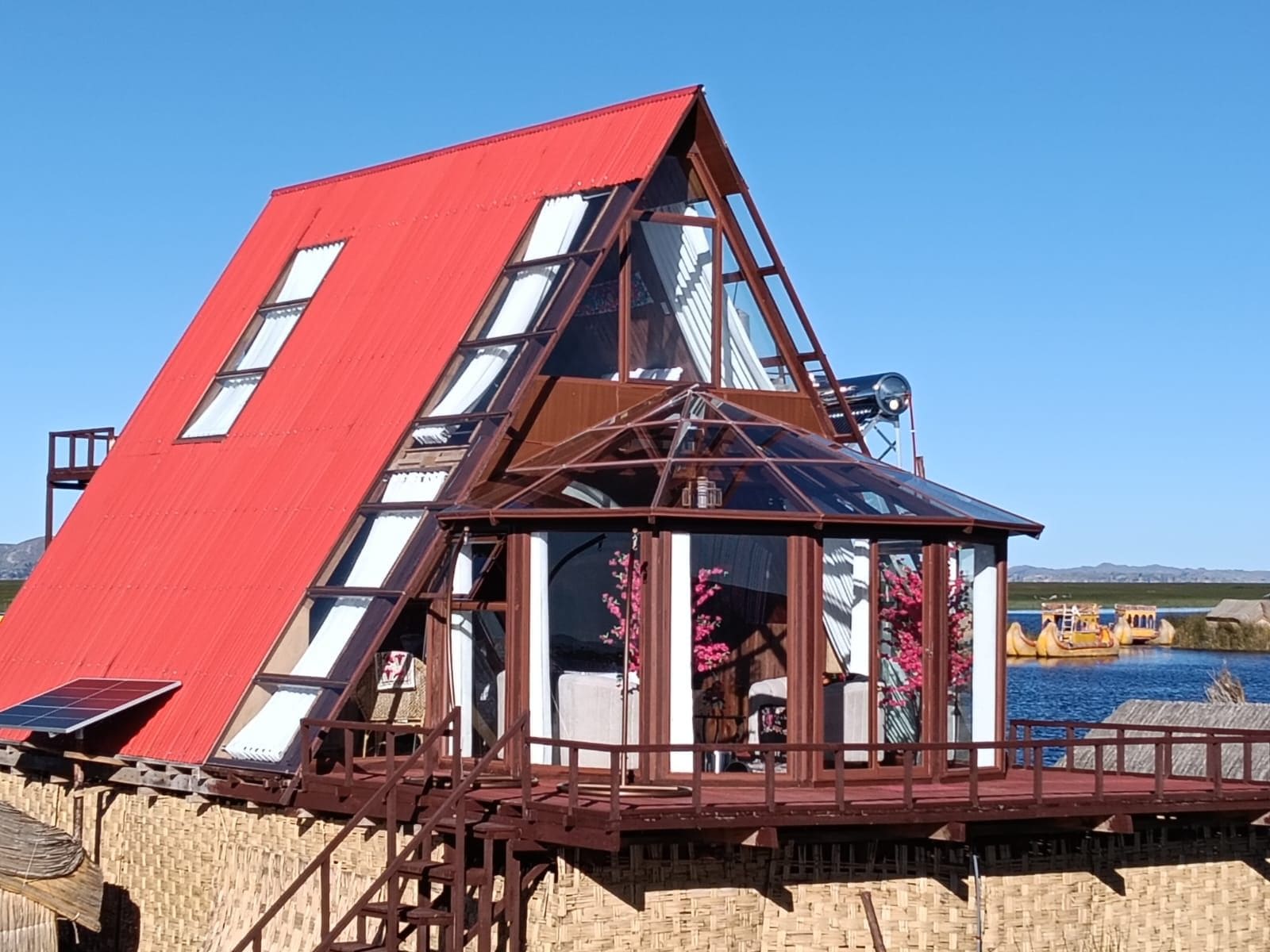 A triangular building with a red roof and multiple windows, situated by a body of water.