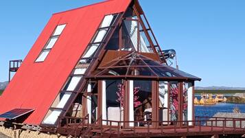 A triangular building with a red roof and multiple windows, situated by a body of water.