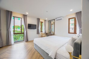 Moderni hotellihuone, jossa on suuri sänky, työpöytä, tuoli, televisio ja parveke, jossa on verhot.