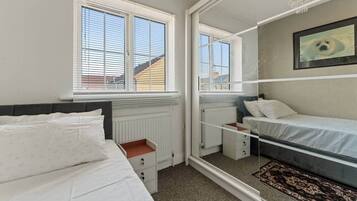 A bedroom with two beds, a radiator, a window, and a mirror reflecting the room.
