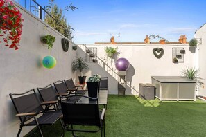Een dakterras met een tafel en stoelen, een klein tuintje met kunstgras, en diverse planten in potten.