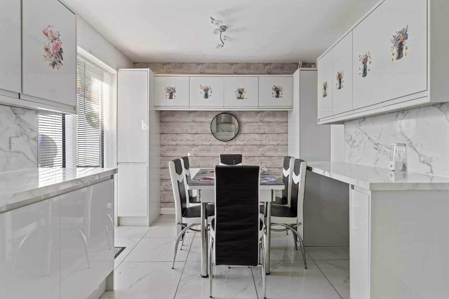 Una cocina moderna con armarios blancos, encimera de mármol y un comedor con mesa y sillas redondas.