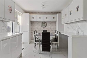 Una cocina moderna con armarios blancos, encimera de mármol y un comedor con mesa y sillas redondas.