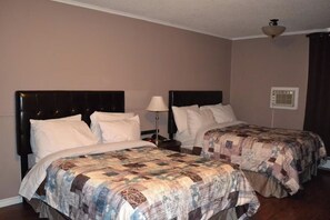 Een hotelkamer met twee bedden, elk met hoofdeinde en een gewatteerde spreidekker. Daartussen staat een nachtkastje met een lamp.