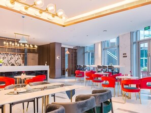 Un espace repas moderne avec des chaises rouges, une table blanche et un luminaire suspendu au plafond.