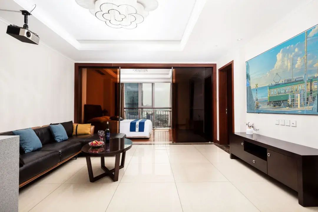 Ein modernes Wohnzimmer mit einer Couch, einem Couchtisch und einem Fernseher. Es gibt einen Balkon mit Blick auf die Stadt.