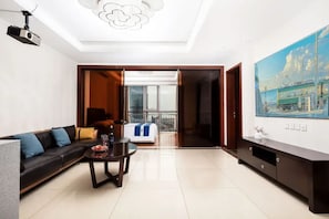 A modern living room with a sofa, a coffee table, and a TV. There is a balcony with a view of the city.