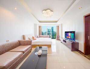 A modern hotel room with a bed, sofa, TV, and a view of the city.