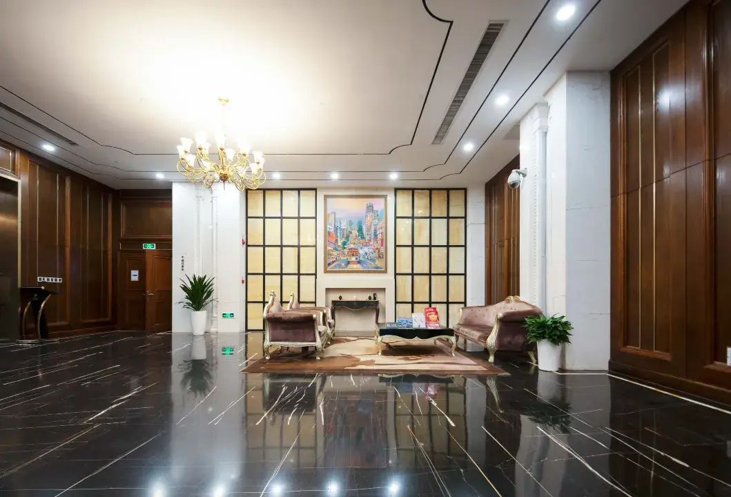 A lobby with a polished floor, a chandelier, seating area, and a painting on the wall.