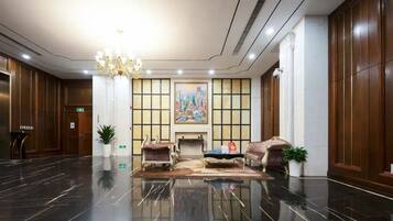 A lobby with a polished floor, a chandelier, seating area, and a painting on the wall.