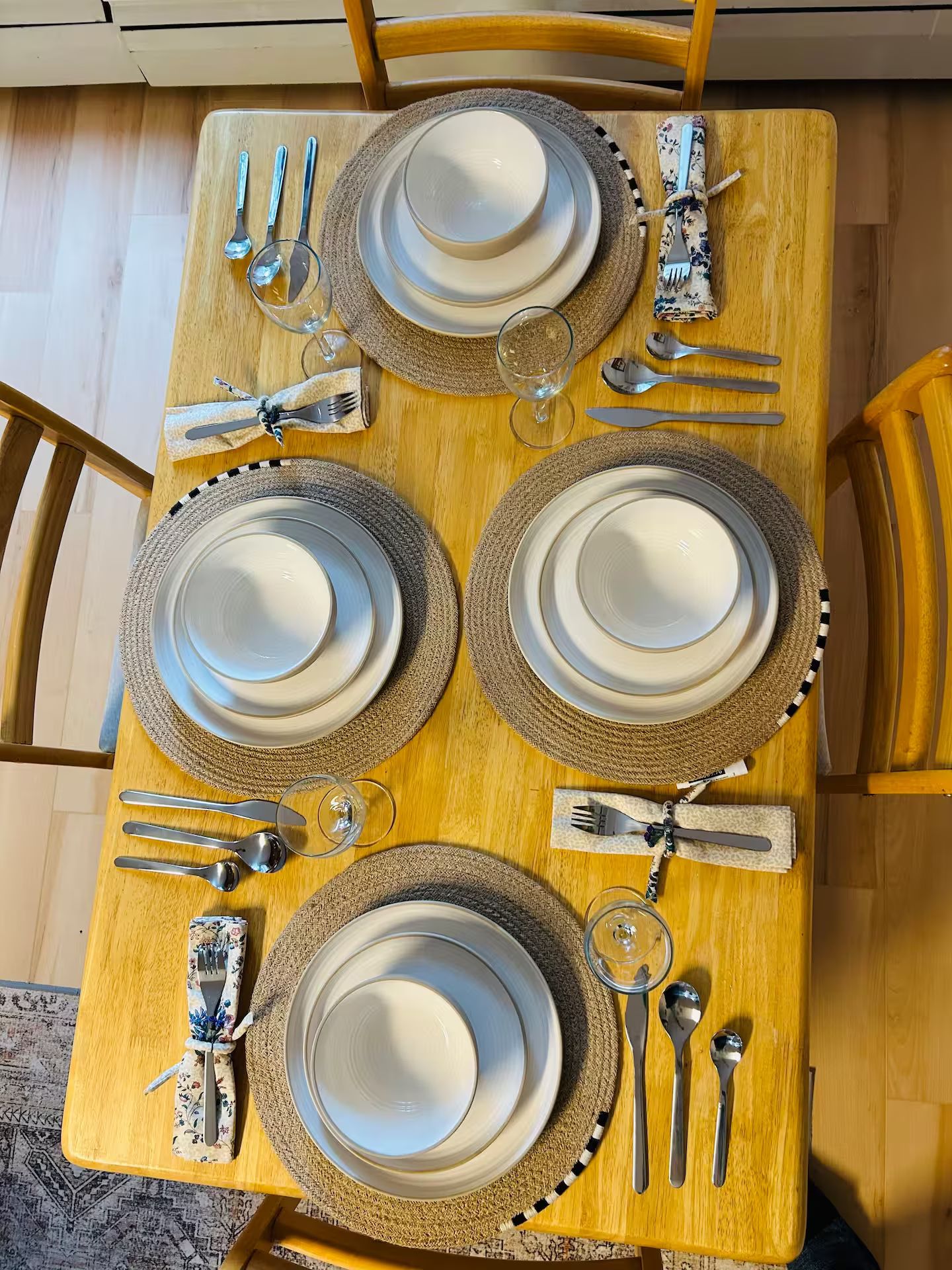 A dining table set with four plates, cutlery, and glasses, surrounded by chairs.