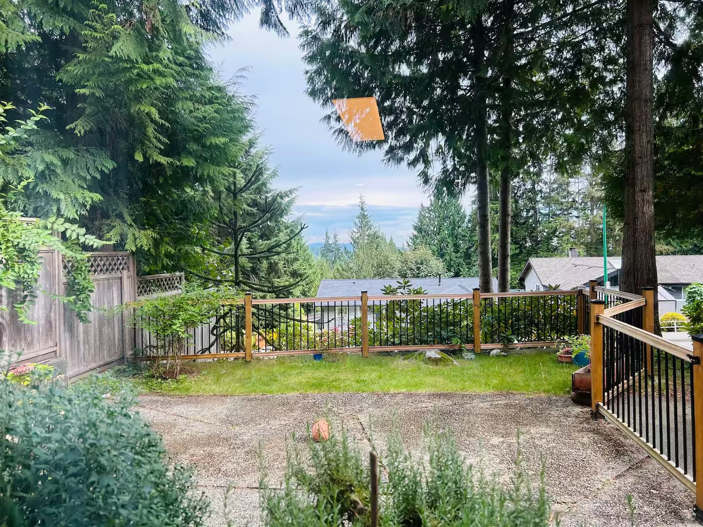 Une cour arrière clôturée avec un espace recouvert de gravier, une terrasse en bois et une vue sur une zone boisée.