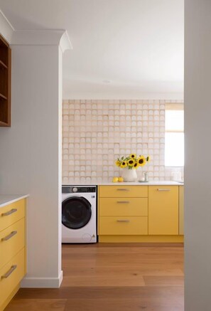 A kitchen with a washing machine, yellow cabinets, and a tiled backsplash. - Kleopatra Retro Coastal Luxury with Ocean Views (Sunshine Coast)