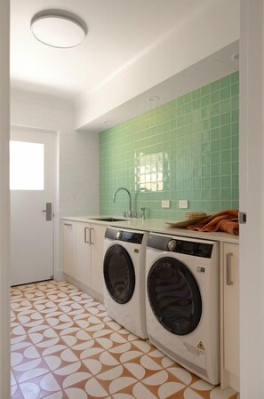 Un lavadero con dos lavadoras, un lavamanos y una pared de azulejos verdes.