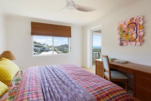 Un dormitorio con cama, escritorio, silla, ventana con vistas y ventilador de techo.