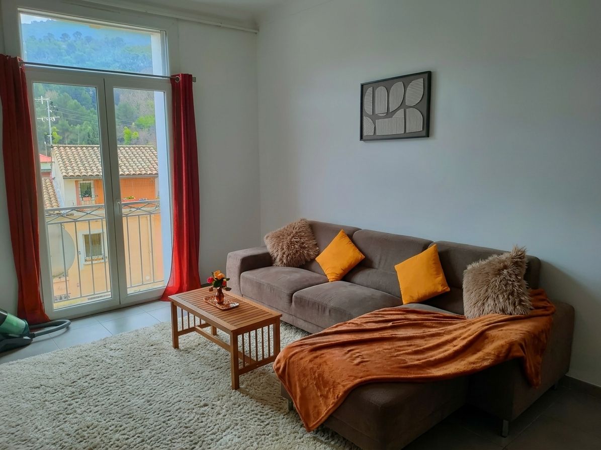 Un soggiorno con un divano, un tavolino, una coperta e una finestra con tende.