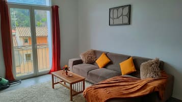 Un soggiorno con un divano, un tavolino, una coperta e una finestra con tende.