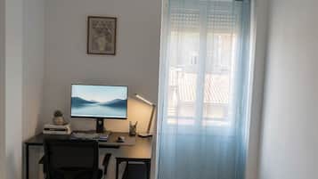 Una stanza con una scrivania, un computer e una sedia, una finestra con tenda e un quadro appeso al muro.