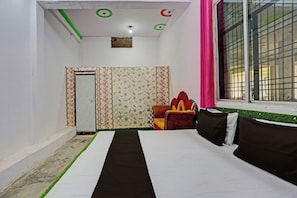 A room with a bed, a window with a view, a door, and a small window with a grid pattern. - Hotel O Jai Bhole Guest House And Rooms (Rasulabad)