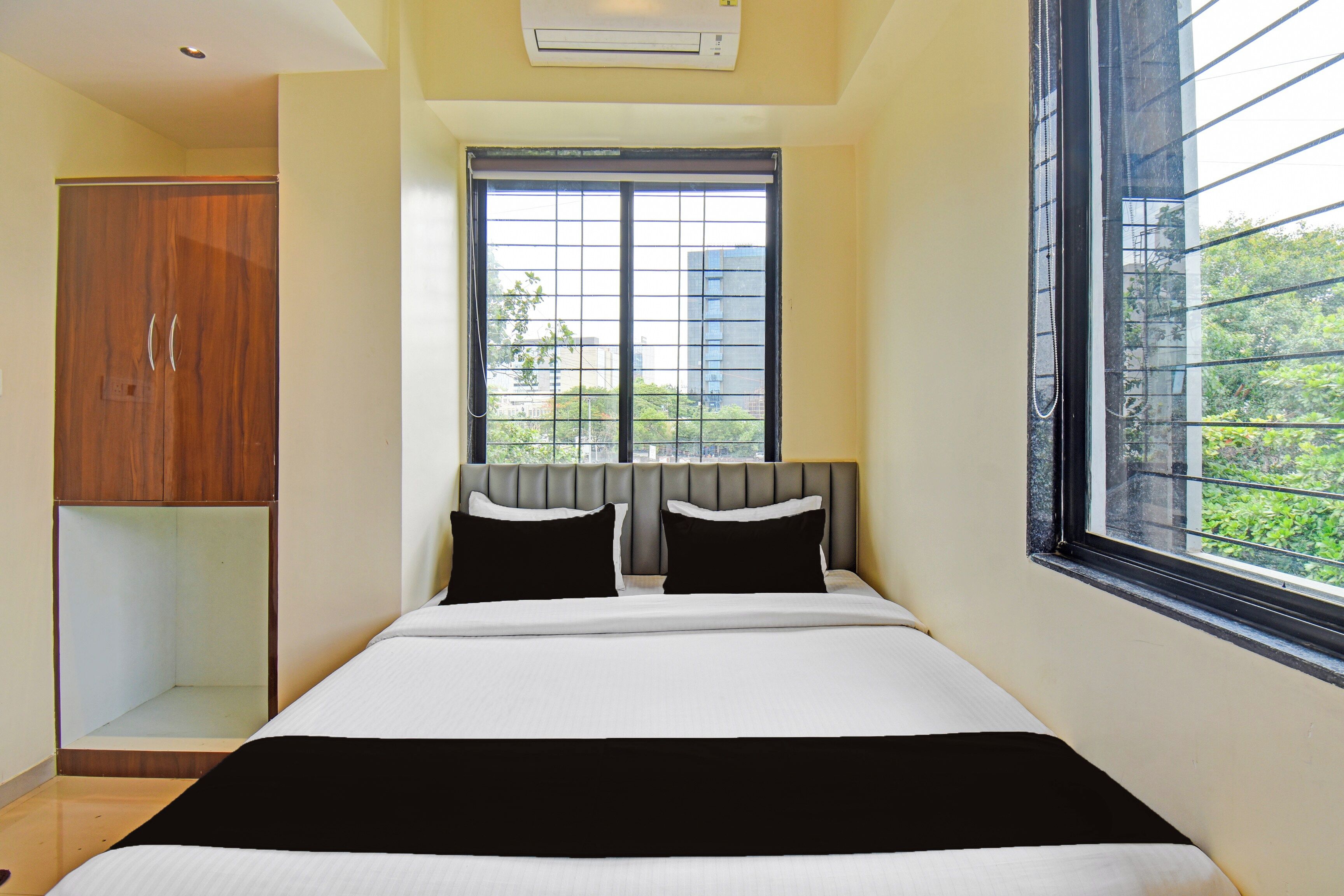 Une chambre d’hôtel équipée d’un lit, d’une armoire, d’une fenêtre donnant sur des immeubles et d’un appareil de climatisation.
