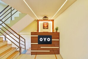 A reception desk with a sign that reads 'OYO' in a modern interior with a staircase and a ceiling fan. - Hotel O RVC GRAND CENTRAL (Pune)