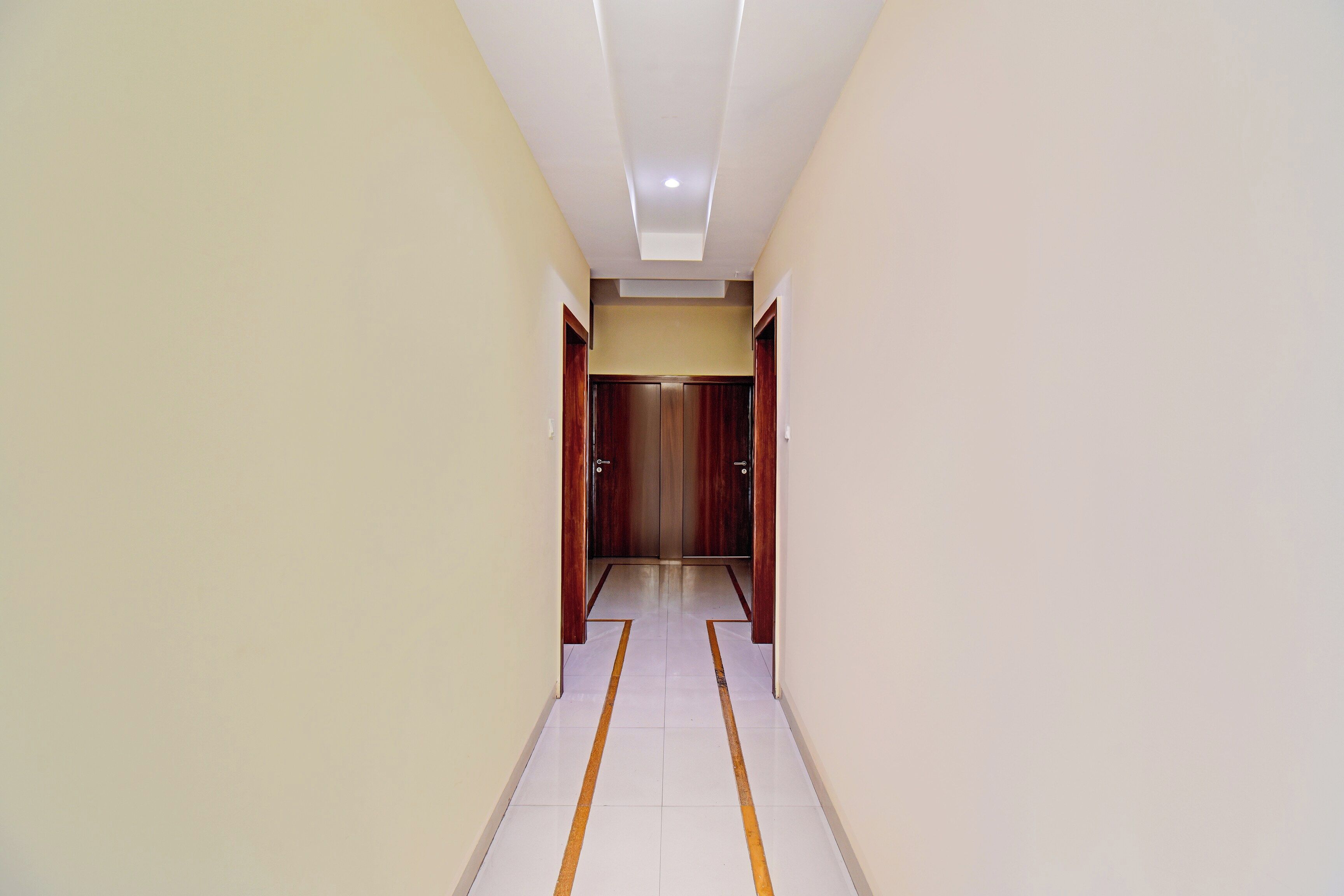 Un couloir avec un luminaire au plafond, une porte au fond et un sol marqué d’une ligne jaune.