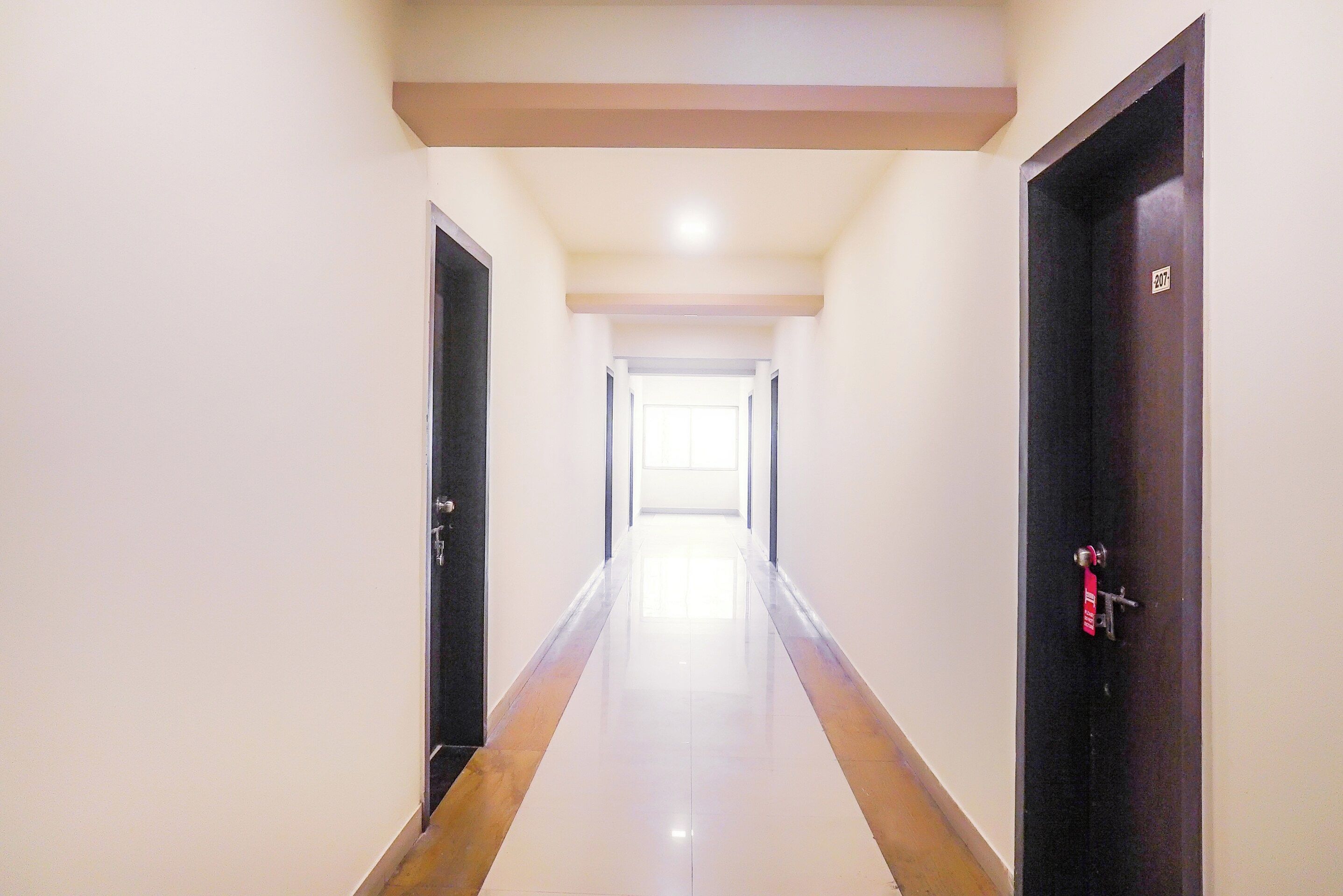 A long, narrow hallway with a reflective floor, leading to a bright room at the end.