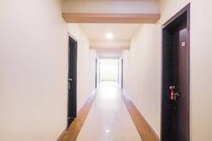 A long, narrow hallway with a reflective floor, leading to a bright room at the end. - Hotel O Paradise Inn Talegaon Dabhade (Mawal)