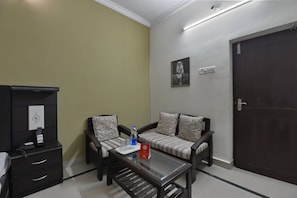 A room with a sofa set, a coffee table, a cabinet with a remote control, and a door. - Hotel O Sai Leela (Puri)