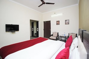 A hotel room with a bed, a television, a ceiling fan, a door, and two chairs. - Hotel O Sai Leela (Puri)