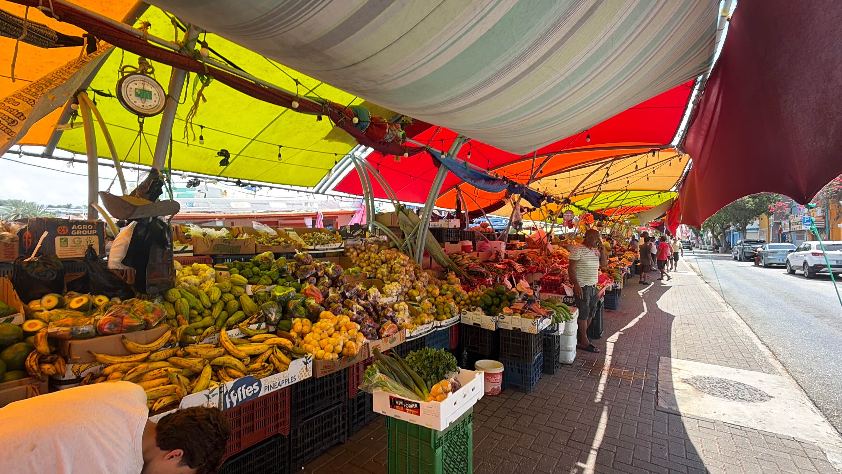 Een open markt met verschillende soorten fruit en groenten, gepresenteerd op tafels onder kleurrijke partytenten.