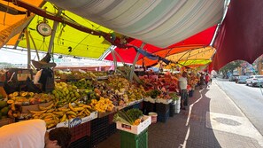 Un mercado al aire libre con diversas frutas y verduras exhibidas sobre mesas bajo coloridos toldos.