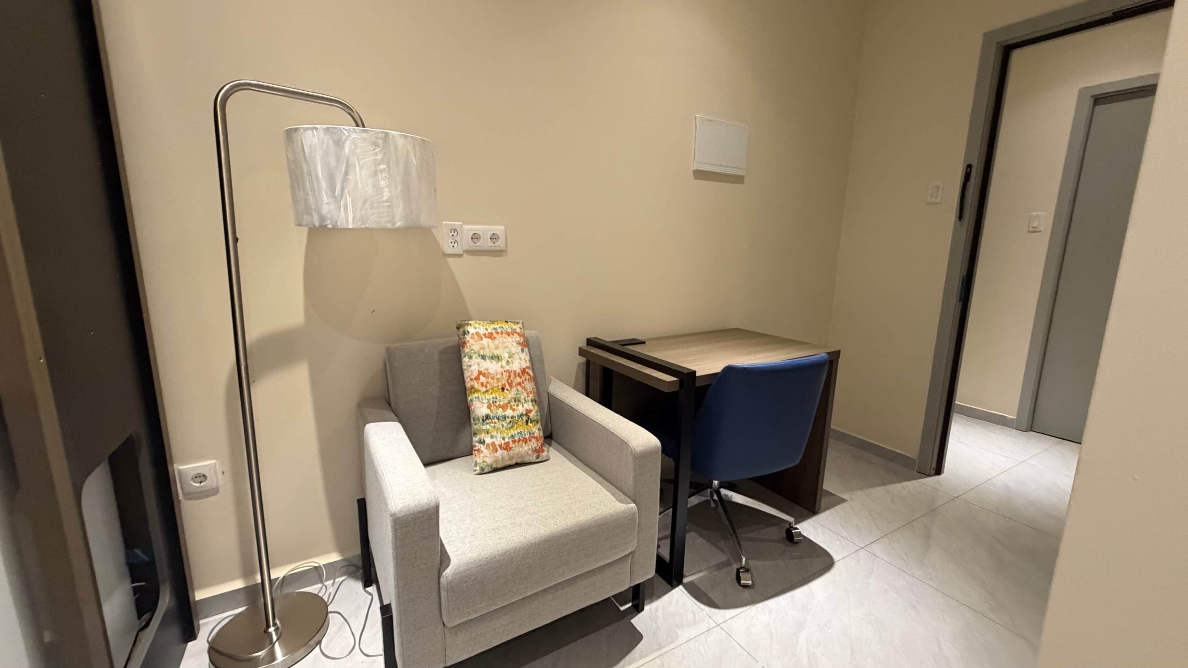 Una habitación pequeña y moderna con un sofá gris, una silla azul, una mesa de madera y una lámpara de pie.