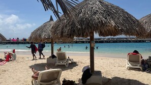 A beach with thatched umbrellas, lounge chairs, and a calm sea. - The Heart of Punda King Studio (Willemstad)