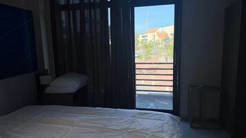 Un dormitorio con cama, almohada, ventana y vistas al exterior.
