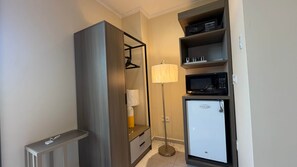 Una kitchenette compacta con microondas, un refrigerador pequeño y una lámpara de pie.