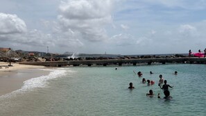 Una playa con agua cristalina, un muelle y gente nadando.