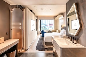 Una habitación de hotel moderna con cama, zona de estar, baño con tocador y un espejo grande.