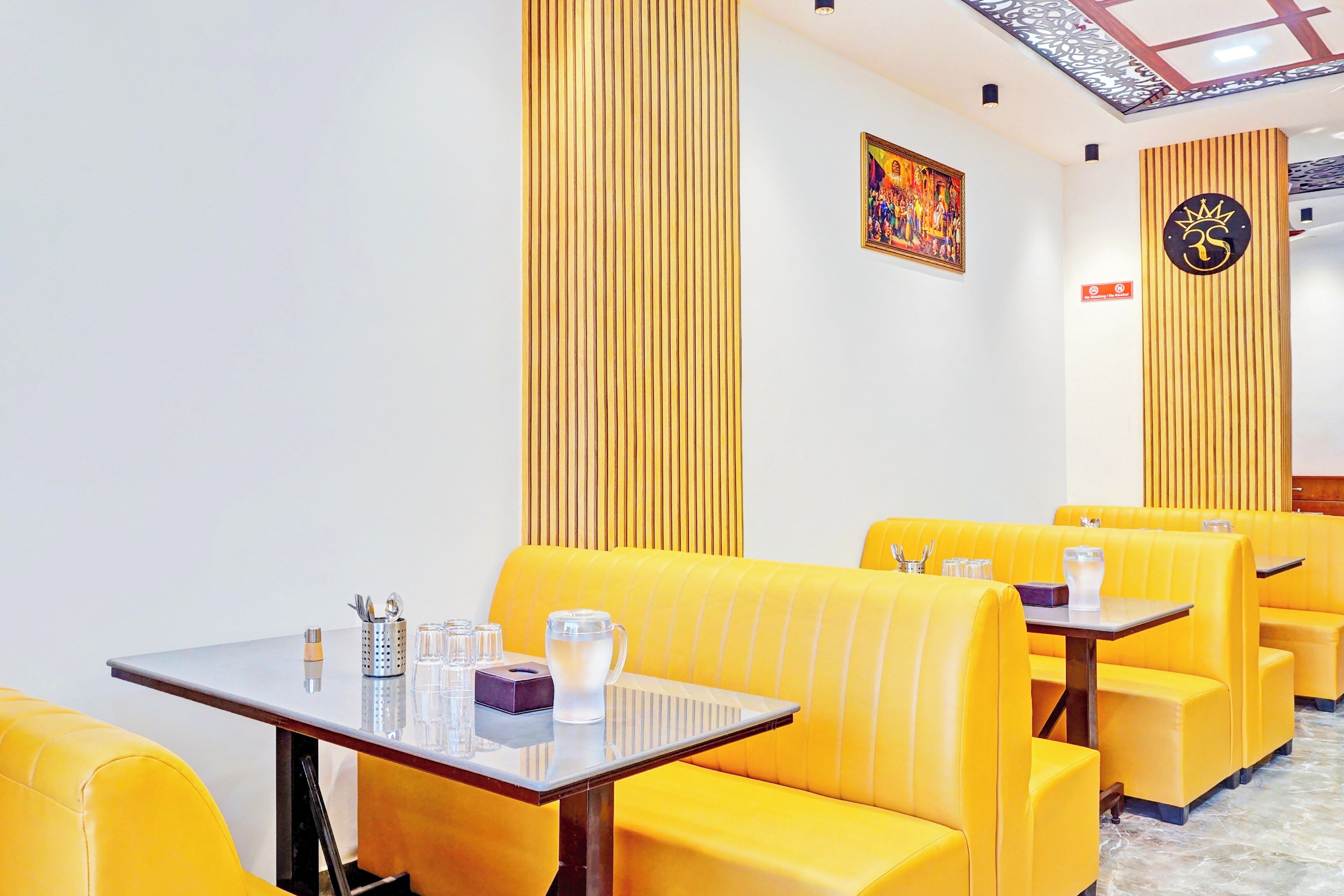 A restaurant interior with yellow booths, a table with cutlery, glasses, and a teapot.