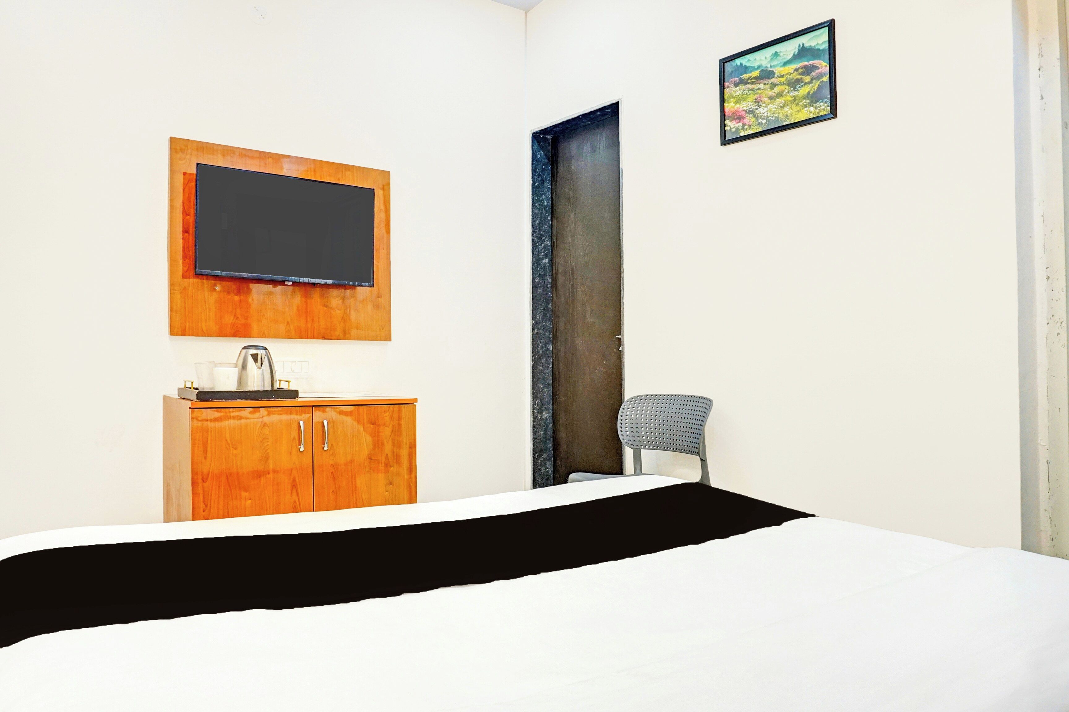 A room with a bed, a wooden cabinet, a chair, a television mounted on the wall, and a door.