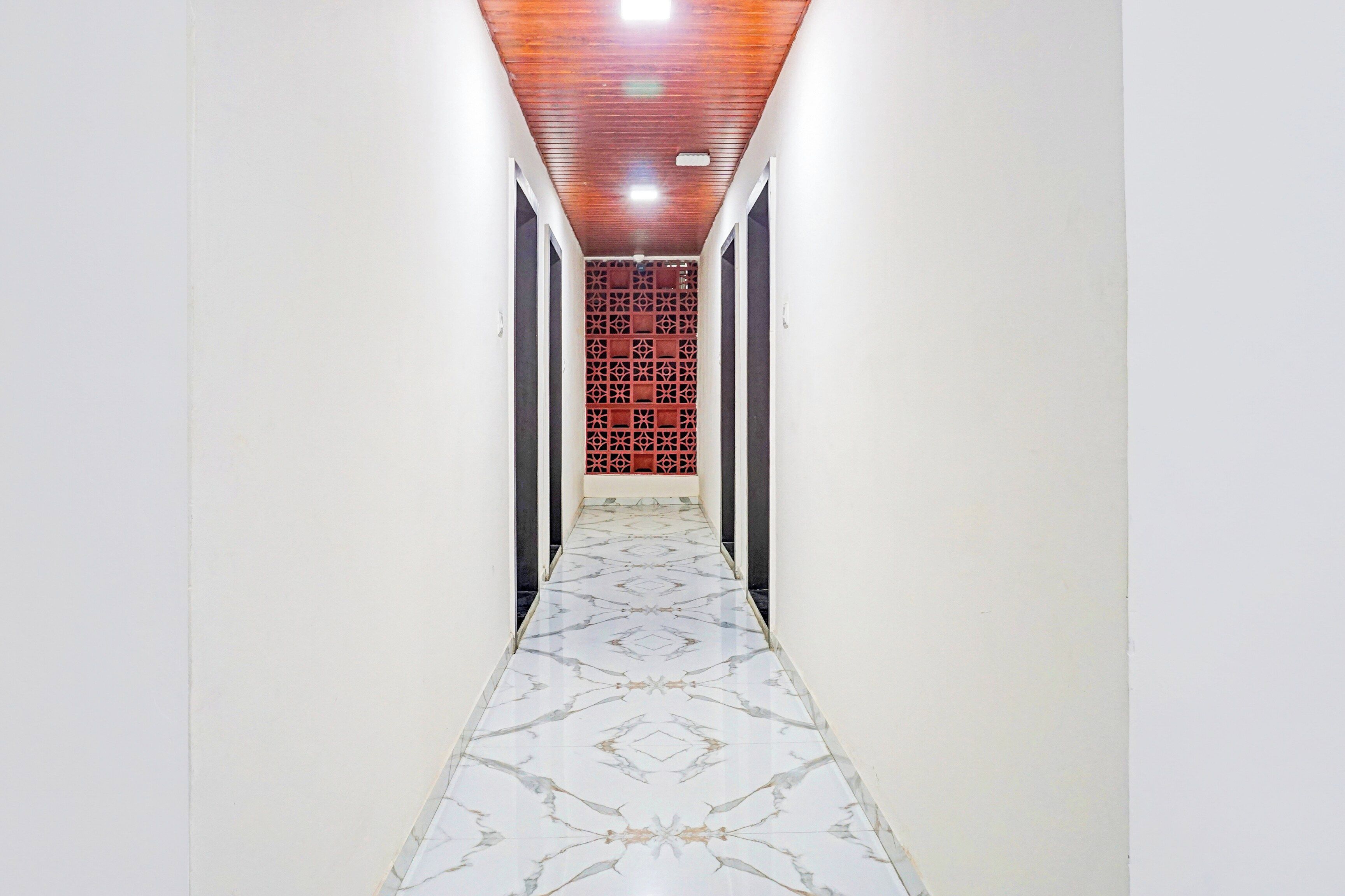 A hallway with a patterned floor, a wooden ceiling, and a red patterned wall at the end.