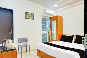 Ein Hotelzimmer mit einem Bett, einem Sessel, einem Schreibtisch mit Wasserkocher und einer Klimaanlage.
