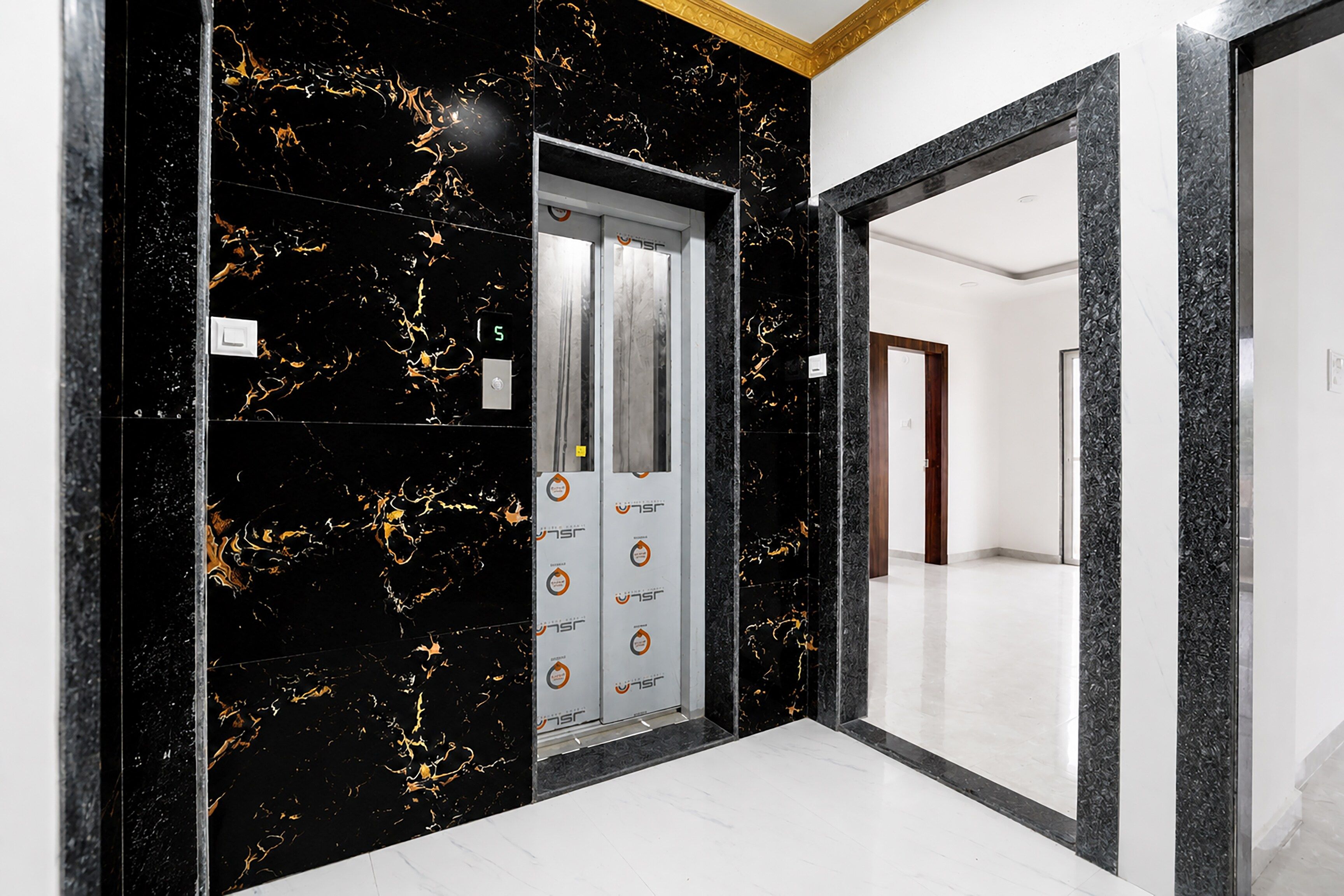 Un couloir avec un mur en marbre noir et une porte blanche dotée d’un écran numérique.