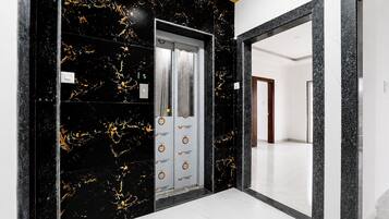 Un couloir avec un mur en marbre noir et une porte blanche dotée d’un écran numérique.