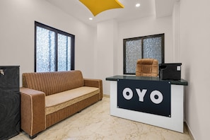 Ein Empfangsbereich mit einer Couch, einem Schreibtisch mit dem Schriftzug 'OYO' und zwei Fenstern mit ornamentbemustetem Glas.