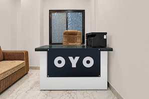 Una recepción con la marca 'OYO', un sillón de cuero marrón y un ventanal con un diseño geométrico.